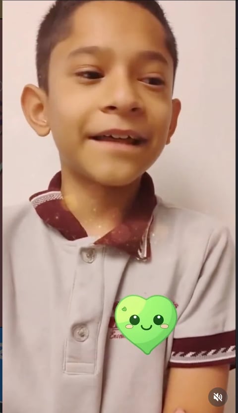 Young boy wearing cream and maroon polo shirt with a green smiling heart emoji overlay on chest